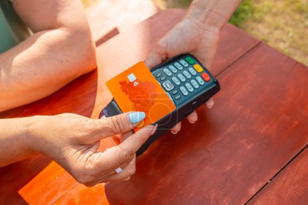 Téléchargez les photos : Femme payer avec carte de crédit. Femme d'âge moyen payant avec carte de crédit dans un café en plein air. - en image libre de droit