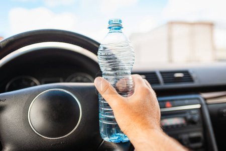 Téléchargez les photos : Main masculine tenant une bouteille d'eau en plastique à l'intérieur de la voiture tout en conduisant une voiture dans le trafic.. - en image libre de droit
