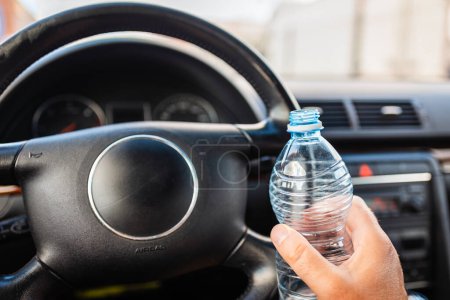 Téléchargez les photos : Main masculine tenant une bouteille d'eau en plastique à l'intérieur de la voiture tout en conduisant une voiture dans le trafic.. - en image libre de droit