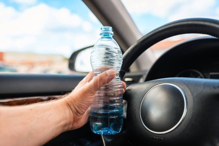 Téléchargez les photos : Mans main tenant bouteille d'eau en plastique à l'intérieur de la voiture tout en conduisant une voiture dans le trafic.. - en image libre de droit