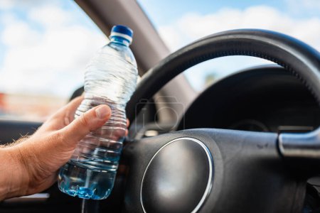 Téléchargez les photos : Mans main tenant bouteille d'eau en plastique à l'intérieur de la voiture tout en conduisant une voiture dans le trafic.. - en image libre de droit