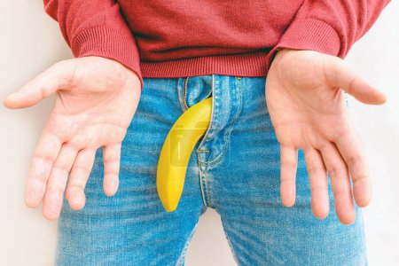 Foto de Impotencia y salud de los hombres. Un hombre abre las palmas de las manos y el plátano cerca de los genitales.. - Imagen libre de derechos
