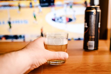 Téléchargez les photos : Les alcooliques qui regardent le sport à la télé à la maison.Les alcooliques.bière fraîche dans un verre de cannette sur la table. - en image libre de droit