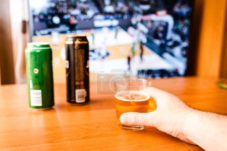 Téléchargez les photos : Les alcooliques qui regardent le sport à la télé à la maison.Les alcooliques.bière fraîche dans un verre de cannette sur la table. - en image libre de droit