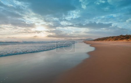 Photo for Wide panoramic view of a pristine beach and ocean waves crushing on the shore during sunset before the storm. Stunning cloudscape and seascape on the Sunshine Coast in Australia. - Royalty Free Image