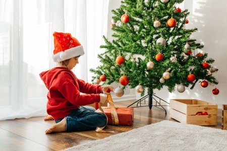 Photo for New Years and Christmas. The boy unties the bow and opens the box with a Christmas present. - Royalty Free Image