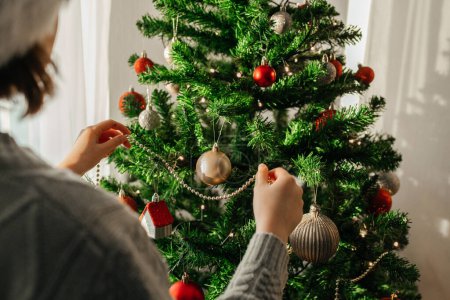 Téléchargez les photos : La fille décore le sapin de Noël pour les vacances. Se préparer pour Noël et le Nouvel An. Les enfants attendent les vacances - en image libre de droit