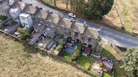 Foto de Foto aérea del hermoso pueblo de East Morton en Keighley en Yorkshire en el Reino Unido, mostrando antiguas hileras históricas de casas adosadas tradicionales por una carretera rodeada de campos de agricultores. - Imagen libre de derechos