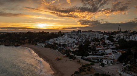Foto de Foto aérea de la hermosa ciudad de Albufeira en Portugal que muestra la playa de arena dorada Praia da Oura, con hoteles y apartamentos con la puesta de sol en el fondo por la noche. - Imagen libre de derechos
