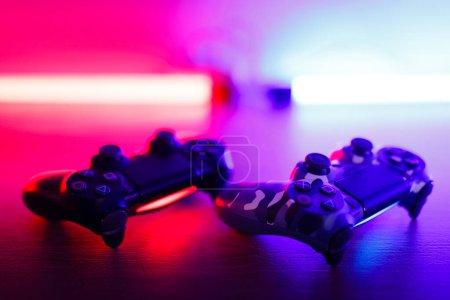 Two gamepads on a wooden table with red and blue backlight.