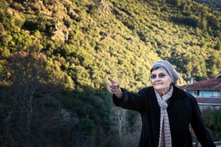 Foto de Mujer anciana con chaqueta negra y sombrero apuntando a las montañas - Imagen libre de derechos
