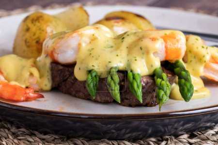 Téléchargez les photos : Une assiette de délicieux steak Oscar aux crevettes géantes et servi avec des pommes de terre rôties. - en image libre de droit