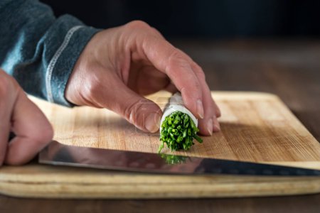 Photo for Hands holding a sharp knife ready for slicing a bundle of chives, on a wooden cutting board - Royalty Free Image