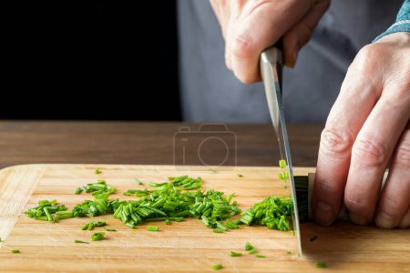 Photo for A close up of a chef slicing fresh chives on a wooden cutting board. - Royalty Free Image