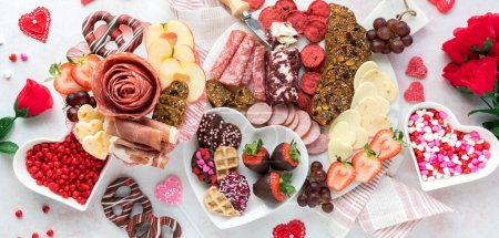 Top down view of a Valentines Day charcuterie arrangement with deli meats, cheese and sweets. 