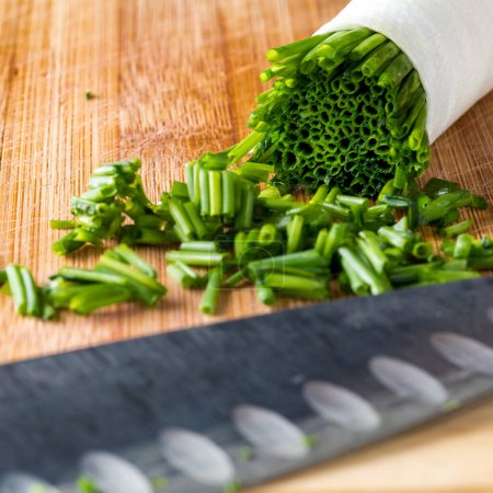 Photo for A bundle of chives with a pile of some freshly chopped in front, on a wooden cutting board. - Royalty Free Image