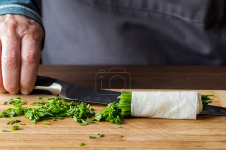 Photo for A chef holding a sharp knife in behind a freshly chopped pile of chives, on a wooden cutting board. - Royalty Free Image