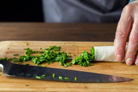 Photo for Chopped chives on a wooden cutting board with a sharp knife on the board in front. - Royalty Free Image