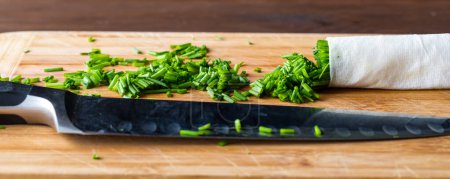 Photo for A narrow view of a pile of chopped chives with a sharp knife in front, all on a wooden cutting board. - Royalty Free Image