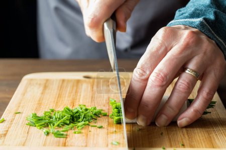 Photo for Close up of a chef using a sharp knife to chop fresh chives, on a wooden cutting board. - Royalty Free Image