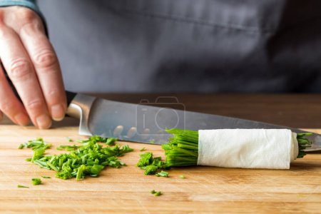 Photo for A hand holding a sharp knife in behind a pile of freshly chopped chives, on a wooden cutting board. - Royalty Free Image