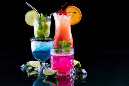 A group of bright colourful cocktails on reflective glass, against a black background. 