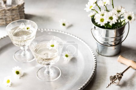Foto de Un primer plano de vino blanco en una bandeja de plata con pequeñas flores de margarita blanca. - Imagen libre de derechos