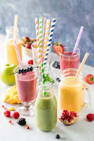 Fresh fruit smoothies with colourful straws surrounded by pieces of fruit and berries.
