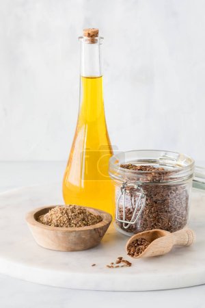 Téléchargez les photos : Un arrangement de graines de lin entières et moulues avec une bouteille d'huile de lin derrière. - en image libre de droit