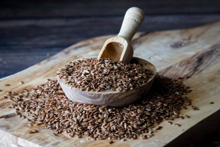 Photo for A small rustic wooden bowl overflowing with whole flax seeds with a small wooden scoop. - Royalty Free Image