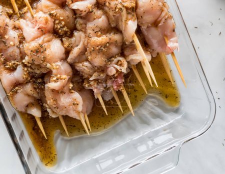 Photo for Above close up view of raw chicken skewers in a glass dish of homemade herbs and spices marinade. - Royalty Free Image