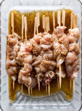 Photo for Above view of a glass dish of chicken breast skewers in a homemade herbs and spice marinade. - Royalty Free Image