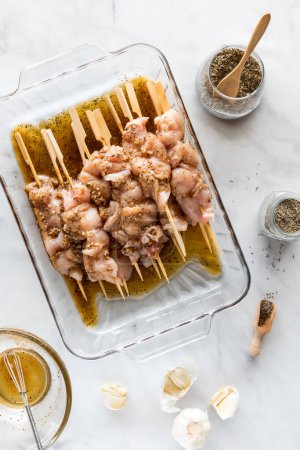 Photo for Chicken skewers marinating surrounded by ingredients including garlic and dried herbs. - Royalty Free Image