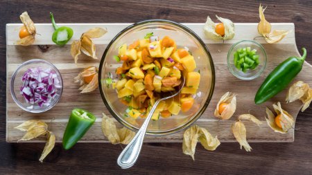 Photo for Above view of a bowl of golden berry and mango salsa surrounded by ingredients used to make it. - Royalty Free Image