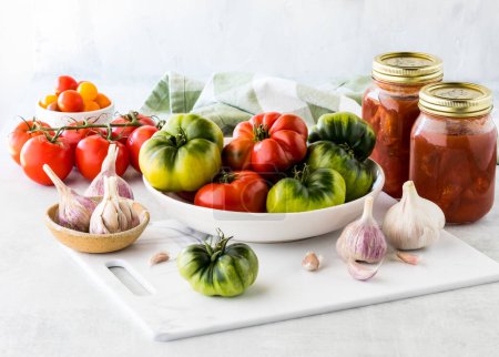 Foto de Un tazón lleno de tomates maduros frescos con frascos de tomates caseros guisados. - Imagen libre de derechos