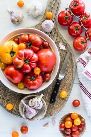A bowl full of various fresh ripe tomatoes on a rustic wooden board. 