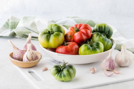 Foto de Una vista de cerca de un tazón lleno de tomates de reliquia recién recogidos, en una tabla de cortar blanca. - Imagen libre de derechos