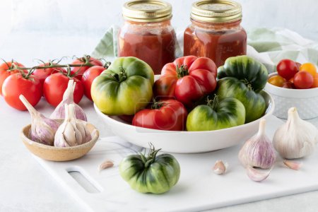 Foto de Un tazón lleno de tomates frescos de la reliquia con los tomates guisados preservados adentro detrás. - Imagen libre de derechos