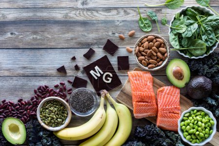 Eine Auswahl an Lebensmitteln mit hohem Magnesiumgehalt mit dem Elementsymbol MG für Magnesium auf der Schokolade und Kopierfläche darüber.