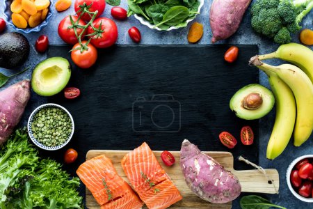 Photo for Healthy fruits, vegetables and fish forming a border around a black slate board. Copy space in the middle. - Royalty Free Image