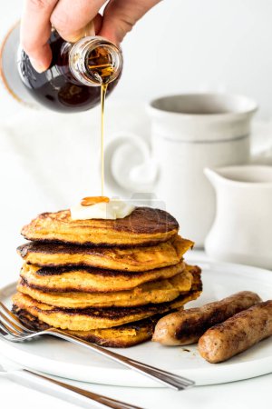 Photo for A close up of a hand pouring syrup on a stack of sweet potato pancakes. - Royalty Free Image