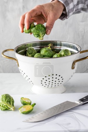 Photo for A colander full of brussel sprouts with a hand reaching in to take a few out for cutting. - Royalty Free Image
