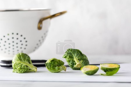Photo for A cutting board topped with brussels sprouts with a colander behind. - Royalty Free Image
