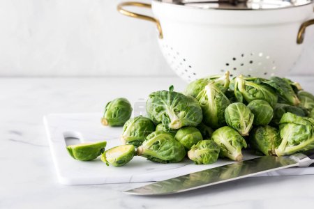 Photo for Brussels sprouts on a cutting board with a knife in front and a colander in behind. - Royalty Free Image