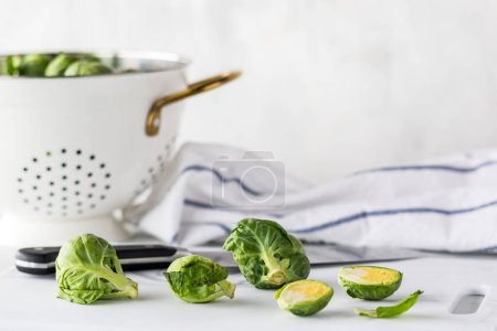 Photo for Fresh raw brussels sprouts on a cutting board with a colander full in behind. - Royalty Free Image