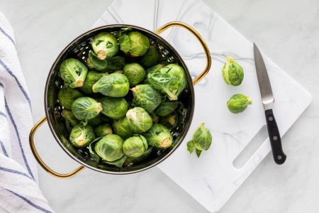 Photo for A colander full of fresh raw brussels sprouts with a few to the side on a cutting board. - Royalty Free Image
