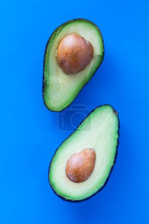 Above view of cut avocados with the seed in the middle, against a bright blue background. 