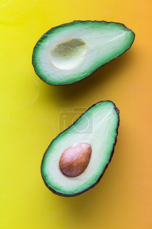 Above view of a freshly cut avocado against a yellowy orange background. 