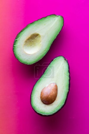 Above view of a ripe avocado cut in half, against a bright pink background.
