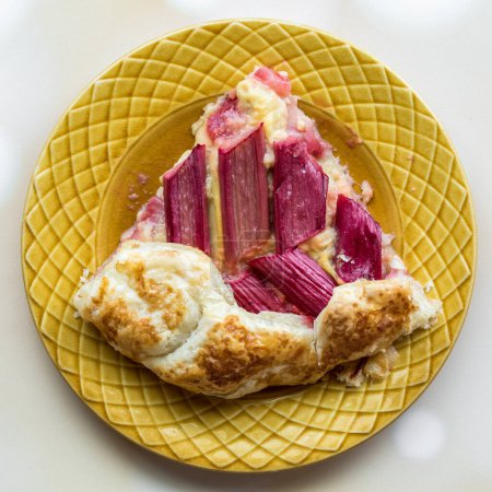 Vue du haut vers le bas d'une tranche de rhubarbe et galette de crème anglaise sur une assiette, prête à manger. 